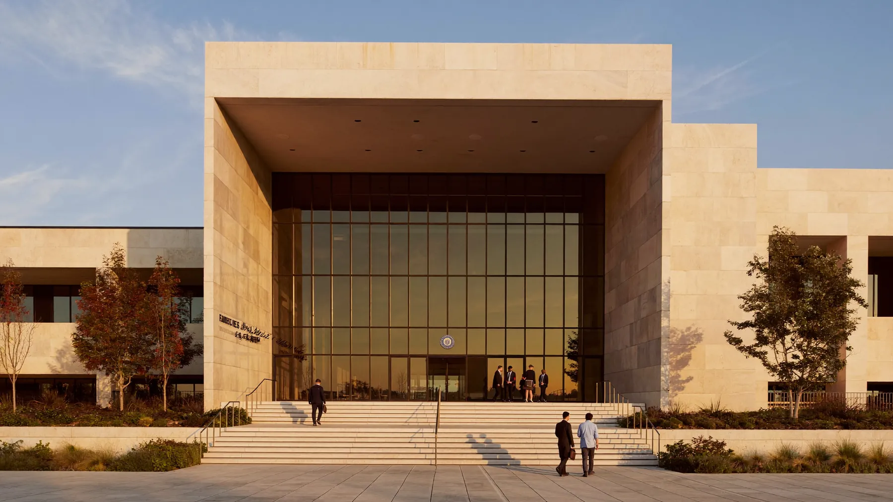 The exterior of a modern civic government building at golden hour with people walking on the steps