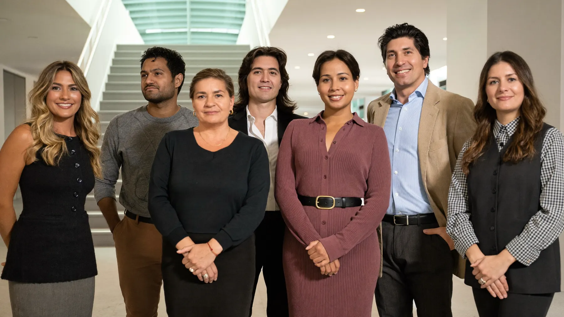 A leadership cohort of nine people of many nationalities standing in a bright atrium