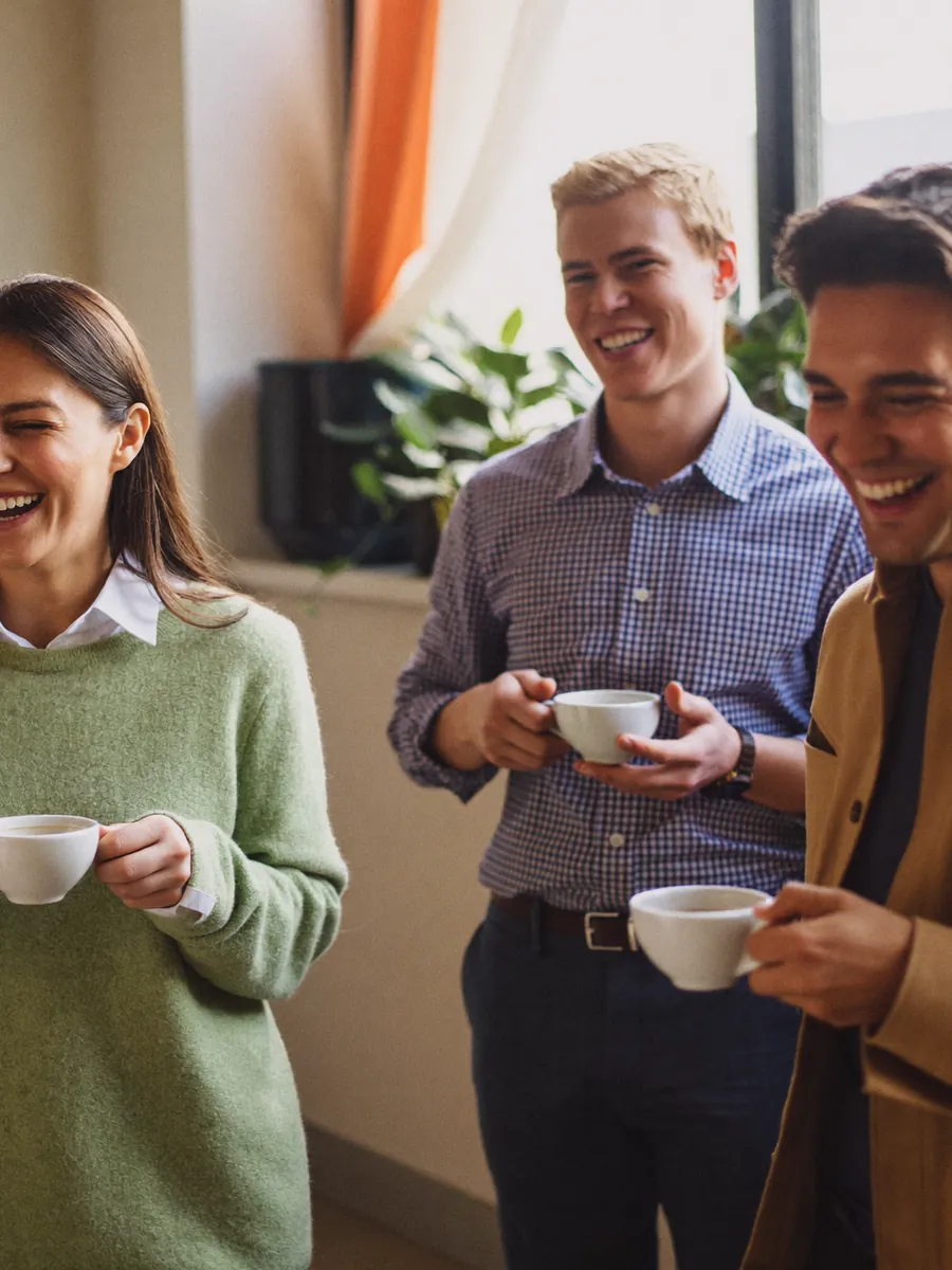 Colleagues laughing together over coffee in an office break area