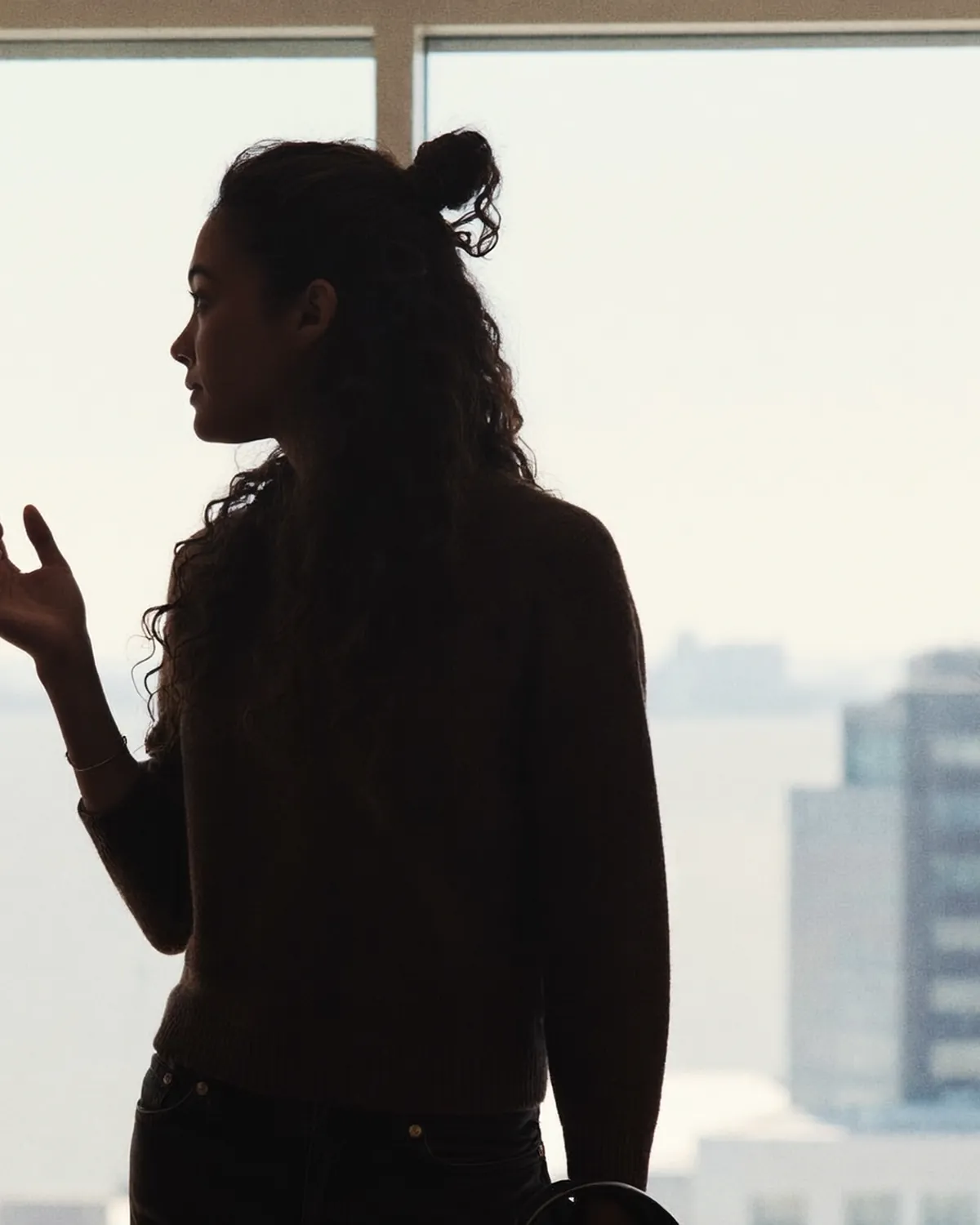 Two people in near-silhouette in conversation against a bright floor-to-ceiling window