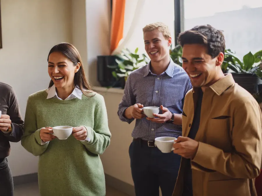Colleagues laughing together over coffee in an office break area