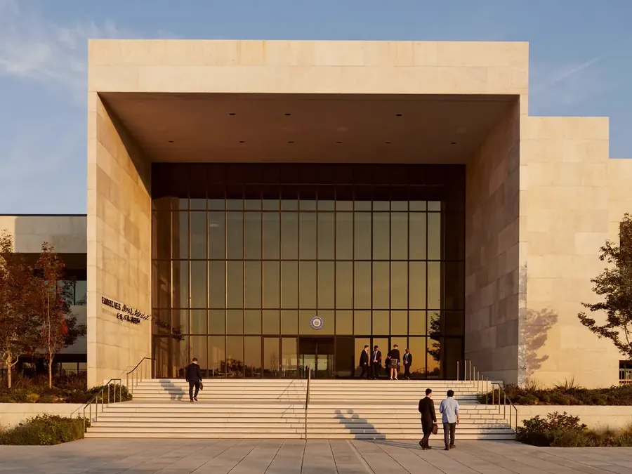 The exterior of a modern civic government building at golden hour with people on the steps