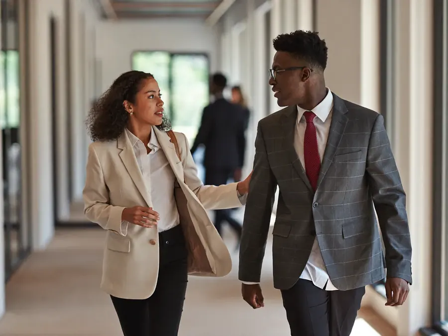 Two colleagues walking and talking in a bright office corridor