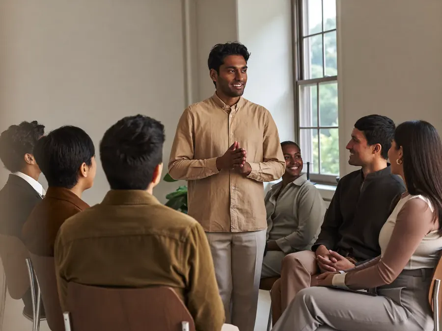 A man presenting to a small semicircle of colleagues in a bright meeting room
